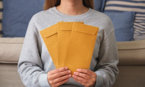 Hands holding three plain brown envelopes