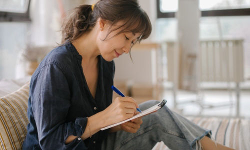  Woman sits on the bed while writing in a notebook