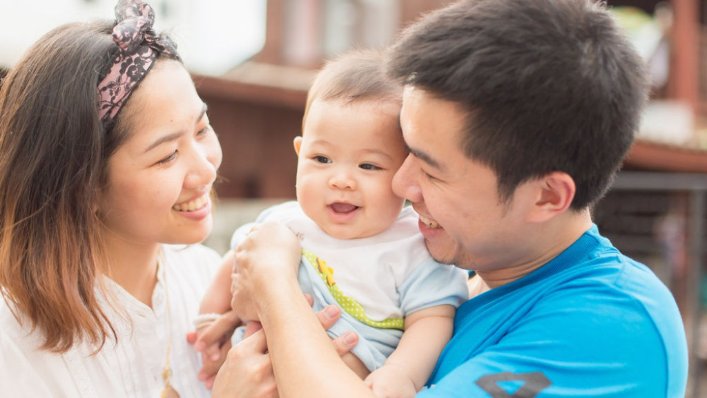 Young Asian couple hold and smile at their baby.