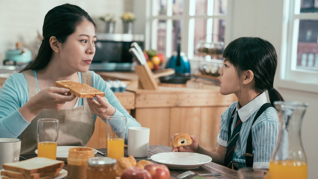 Asian mom talks to her school-age daughter over breakfast.