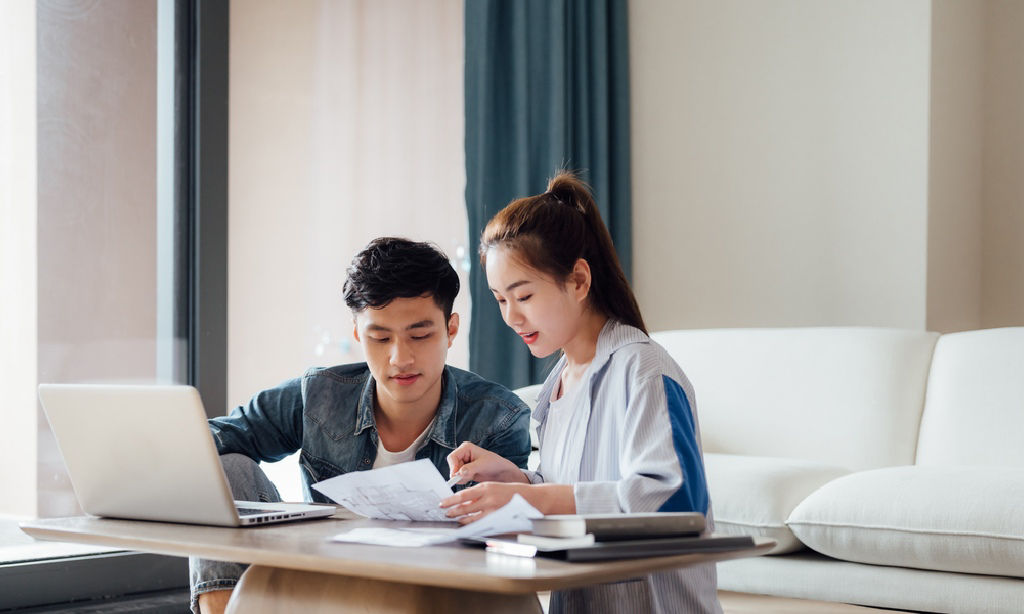 A young Asian couple goes over documents in their living room.