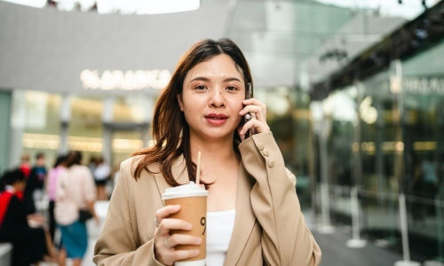 Young Asian professional talks on her smartphone while holding a cup of coffee.