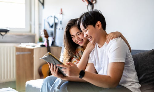 Young smiling Asian couple discuss health insurance while looking at their tablet.