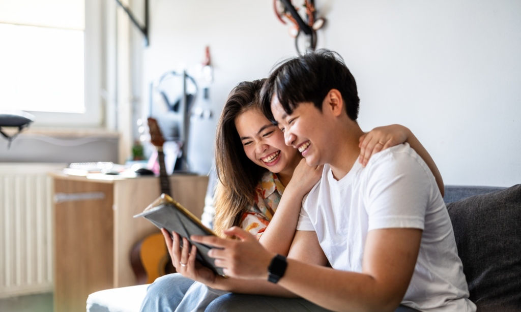 Young smiling Asian couple discuss health insurance while looking at their tablet.