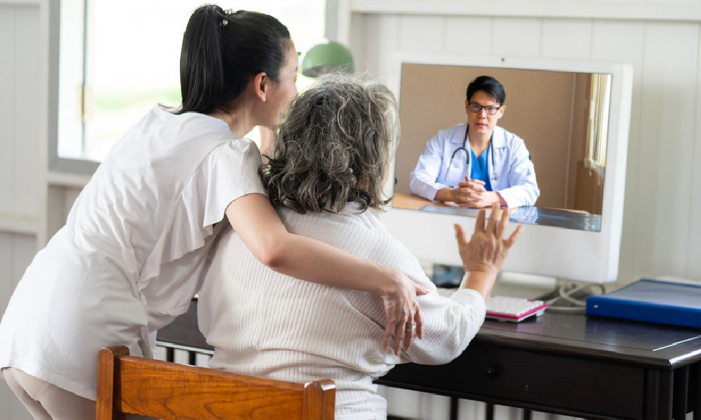 Asian daughter assists her elderly mom during a teleconsultation with a doctor.