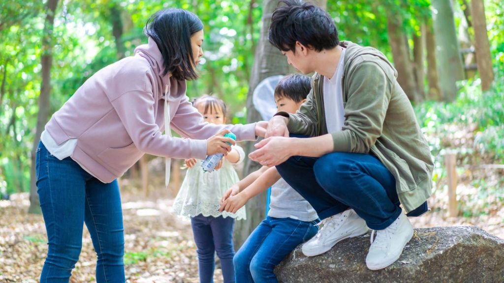 Asian mom sprays insect repellent on her family while walking in the woods.