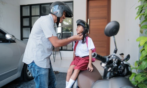 Asian dad puts on daughter’s helmet before they leave for school in a motorcycle.