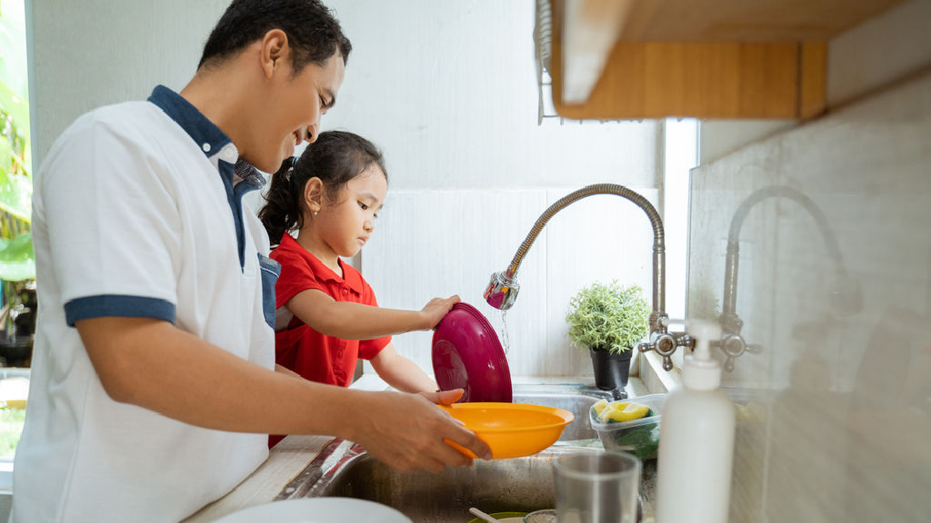 Asian little girl helps her dad wash the dishes.