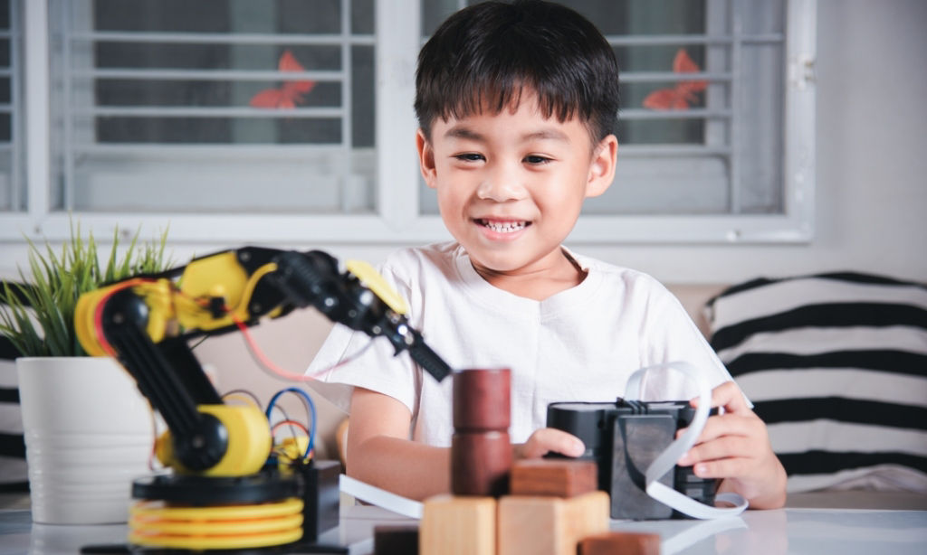 Boy uses a remote-control robotic machine to pick up a wooden block